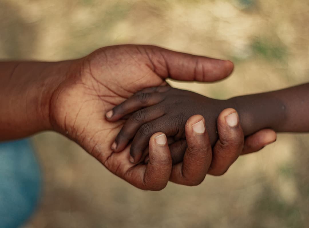 An adult's hand supporting a child's hand — a symbol of protection and solidarity